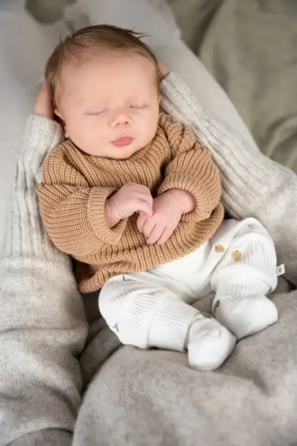 Schattige baby in ribbroek ligt ontspannen op schoot, perfect voor babykleding en comfort.