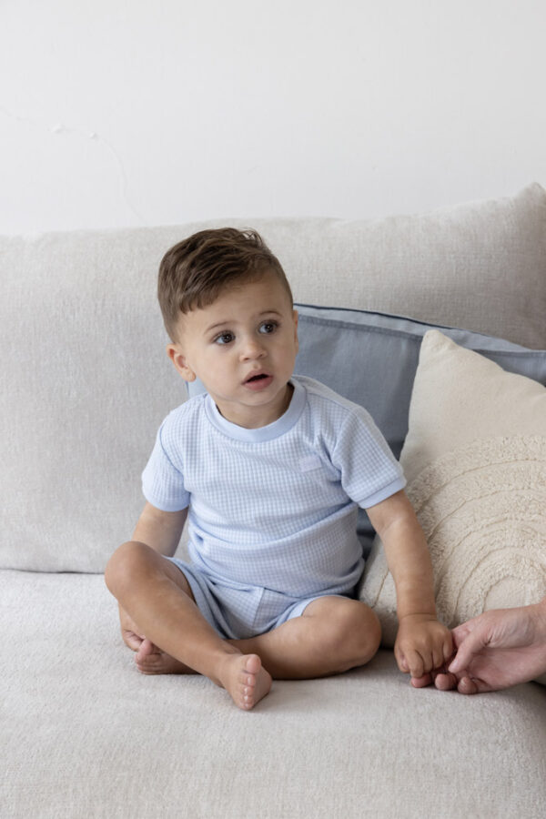 Baby jongen in blauwe wafel shortama zittend op bank.