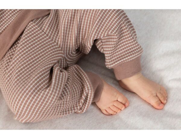 Baby voeten in bruine wafelpyjama, comfortabel en zacht.