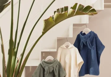 Drie baby badponcho's in grijs, wit en blauw hangen aan een trap.